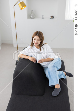 タンブラーを手にソファに座る若い女性 131683080