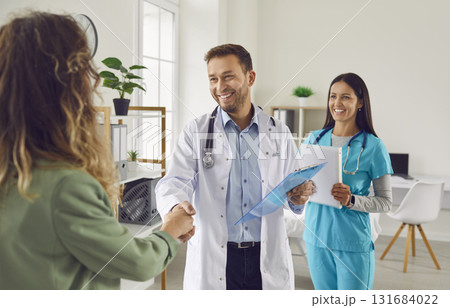 Friendly doctor shaking hands with a young patient standing with nurse in medical clinic Friendly doctor shaking hands with a young patient standing with nurse in medical clinic 131684022