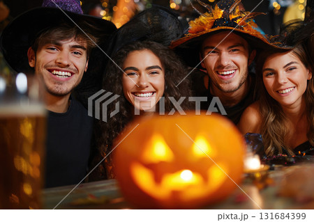 Ai generated friends in witch costumes and hats holding pumpkin celebrating Halloween party at home. 131684399