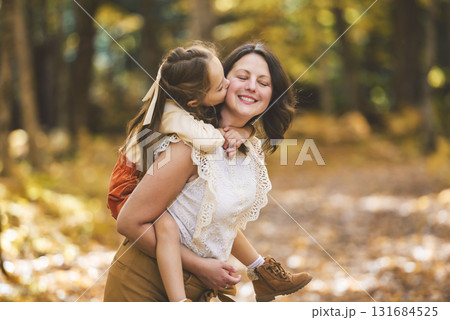 Mature mother giving piggyback ride to small daughter on a walk in autumn forest. 131684525