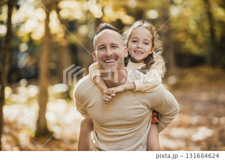 Mature father giving piggyback ride to small daughter on a walk in autumn forest. Mature father giving piggyback ride to small daughter on a walk in autumn forest. 131684624