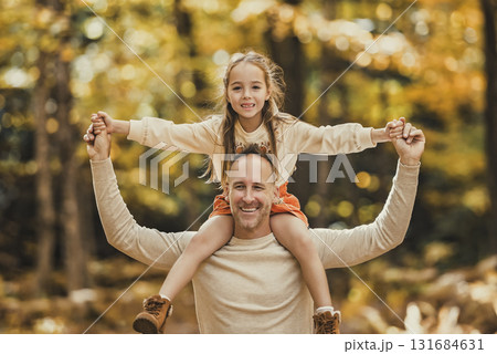 Mature father with daughter on shoulder ride to small daughter on a walk in autumn forest. Mature father with daughter on shoulder ride to small daughter on a walk in autumn forest. 131684631