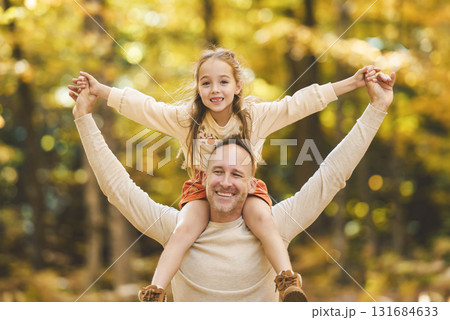 Mature father with daughter on shoulder ride to small daughter on a walk in autumn forest. Mature father with daughter on shoulder ride to small daughter on a walk in autumn forest. 131684633
