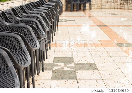 Empty black plastic chairs standing on wet tiled floor after the rain Empty black plastic chairs standing on wet tiled floor after the rain 131684680