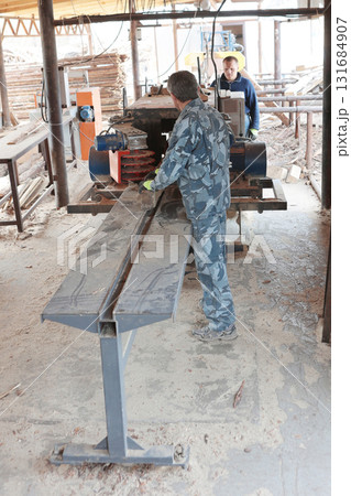 Male worker saws log on machine. Woodworking company. Process of processing logs at sawmill. Sawing tree trunk. Sawmill. Male worker saws log on machine. Woodworking company. Process of processing logs at sawmill. Sawing tree trunk. Sawmill. 131684907