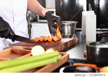 Cook cuts carrots in kitchen. Cooking vegan dish. Cut carrots into strips. Healthy food. Concept of cooking. 131684915