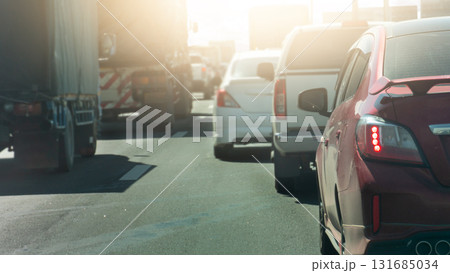 Rear side of red car with turn on brake light. Traffic jam on the road in the city. Blurred background of other cars driving on the asphalt road at bright Moment. Rear side of red car with turn on brake light. Traffic jam on the road in the city. Blurred background of other cars driving on the asphalt road at bright Moment. 131685034