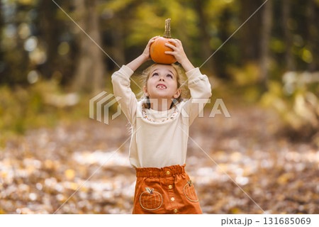 happy child girl throws autumn leaves and laughs outdoors with pumpkin on head happy child girl throws autumn leaves and laughs outdoors with pumpkin on head 131685069
