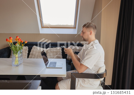 Man using smartphone while working with laptop at home office. Concept of remote work, online communication, fintech, digital banking, e-commerce, productivity and technology 131685431