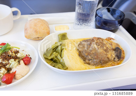 おいしい近距離線ビジネスクラスの機内食の肉料理のハンバーグとサラダ 131685889