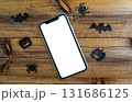 Mockup, smartphone, paper black bat, spiders and pumpkins on wooden background. Halloween background. 131686125