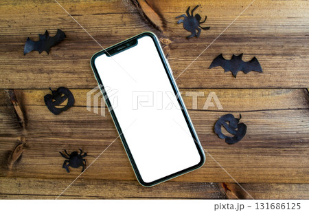 Mockup, smartphone, paper black bat, spiders and pumpkins on wooden background. Halloween background. Mockup, smartphone, paper black bat, spiders and pumpkins on wooden background. Halloween background. 131686125