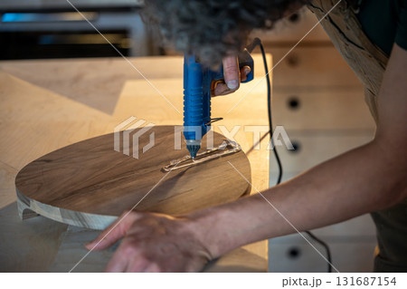 Man sealing cracks on finished wooden item with hot silicone to prepare for epoxy resin filling 131687154