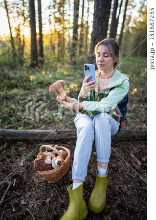 Happy woman backpacker photographing white mushroom from full basket in forest, social media share Happy woman backpacker photographing white mushroom from full basket in forest, social media share 131687285