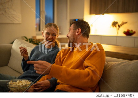 Smiling young couple enjoying popcorn watching movie together on living room sofa, family night 131687407