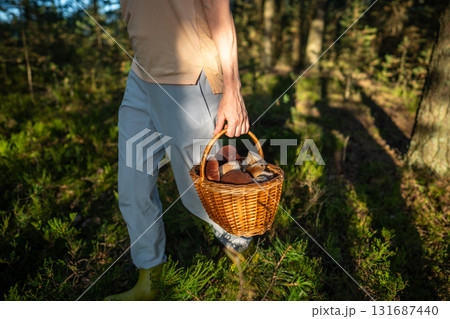 Woman moving along woodland path with full wicker basket with boletus mushrooms during autumn 131687440