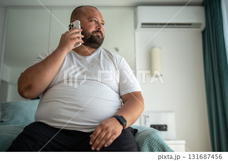 Fat guy calls on phone, sitting on bed, looking out window, signs up for gym to put figure in order 131687456