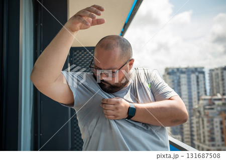 Overweight man suffering from heat, over sweating in summer standing on balcony in summer. 131687508