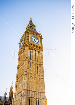 Big Ben, a famous clock tower in London, showcases its intricate architecture. The sky is clear, and the structure reflects sunlight, highlighting its iconic features. 131688288