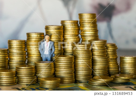 Miniature businessman standing among stacks of euro coins symbolizing finance, wealth, and success Miniature businessman standing among stacks of euro coins symbolizing finance, wealth, and success 131689453