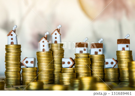 Miniature houses on stacked gold coins symbolizing real estate investment and property value 131689461