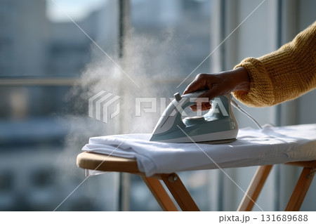 Steam iron applied to a shirt on an ironing board near a window in a bright room 131689688