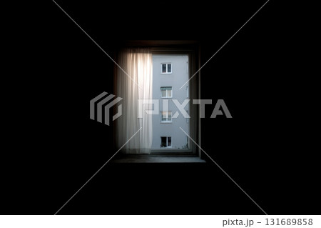 Light filters through a curtain, revealing a building across the street at dusk 131689858