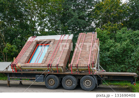 Prefabricated brick wall panels with windows transported on flatbed truck at construction site 131690408