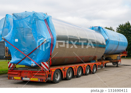Large stainless steel industrial tanks on flatbed truck secured with blue covers for transport 131690411