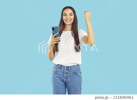 Portrait of happy young woman holding mobile phone, smiling and doing yes gesture Portrait of happy young woman holding mobile phone, smiling and doing yes gesture 131690461