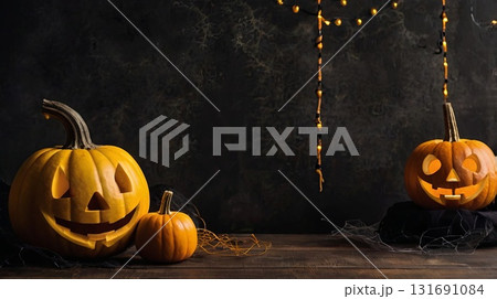 A Halloween backdrop with glowing pumpkins on a dark textured surface and yellow autumn leaves on a dark background. Banner with space for text. 131691084