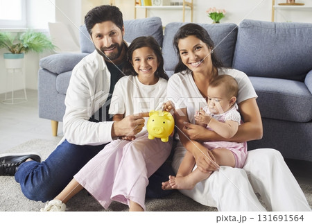 Family with two kids putting money coin into piggy bank sitting on floor at home together. 131691564
