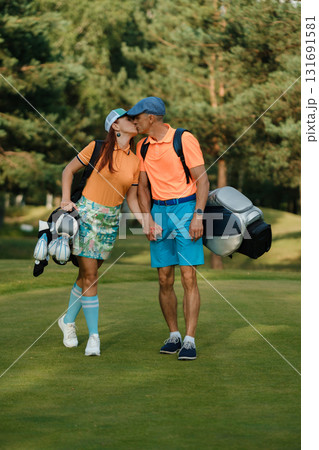 Couple enjoying a romantic moment on the golf course while holding hands and laughing together in vibrant outfits during a sunny day Couple enjoying a romantic moment on the golf course while holding hands and laughing together in vibrant outfits during a sunny day 131691581