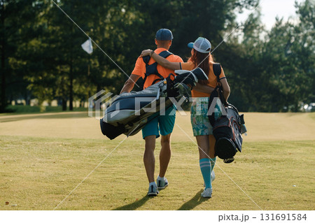 Couple enjoying a sunny day on the golf course while carrying their golf bags and sharing a relaxed moment together 131691584