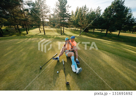 Couple enjoying a sunny afternoon on the golf course while sitting on the green, surrounded by trees and beautifully manicured landscape Couple enjoying a sunny afternoon on the golf course while sitting on the green, surrounded by trees and beautifully manicured landscape 131691692