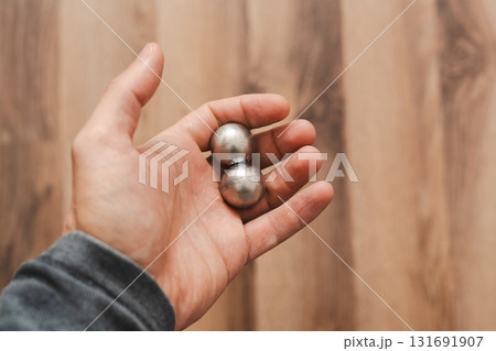 A man's hand holds two CNC metal spheres in warm daylight. A symbol of Earth's poles and the power to control their balance. Precision meets metaphor. 131691907