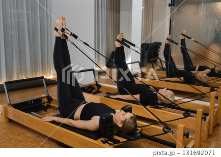 Woman practicing Pilates using reformer equipment in a bright studio during a midday session focusing on core strength and flexibility Woman practicing Pilates using reformer equipment in a bright studio during a midday session focusing on core strength and flexibility 131692071