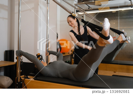 Pilates instructor helping a student with reformer exercises in a well-lit fitness studio during a morning session 131692081