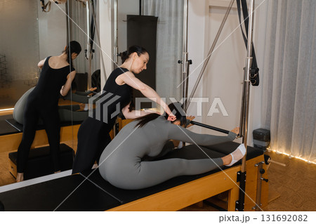 Pilates instructor assists a student in stretching routine in a serene studio setting during a morning class session 131692082