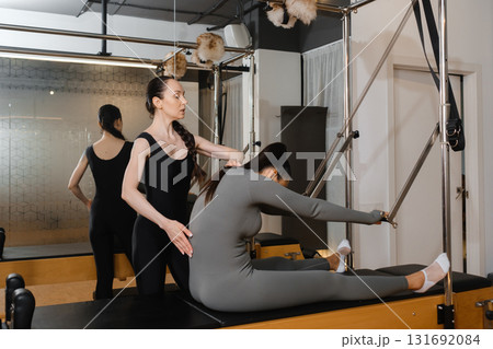 Pilates instructor guiding student on reformer machine during a private session in a modern studio 131692084