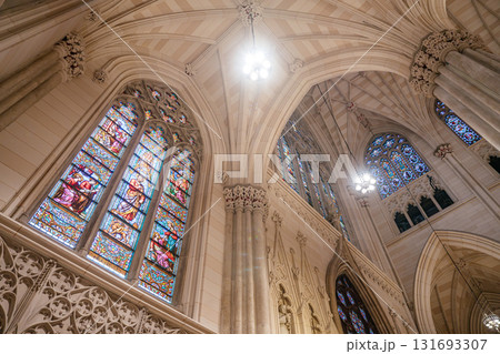 A close-up view of vibrant stained glass windows inside a Gothic-style cathedral. The arched stone architecture and ornate ceiling enhance the sacred and artistic ambiance of the space. A close-up view of vibrant stained glass windows inside a Gothic-style cathedral. The arched stone architecture and ornate ceiling enhance the sacred and artistic ambiance of the space. 131693307