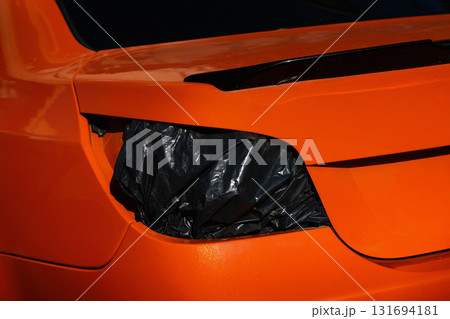 Close-up of an orange car with a broken taillight covered by a black plastic bag. Concept of car, repair, and damage symbolizing maintenance and temporary solution 131694181