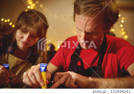 Family Craft Night With Friends: Two Adults Creating Art Under Warm Christmas Lights Family Craft Night With Friends: Two Adults Creating Art Under Warm Christmas Lights 131694261