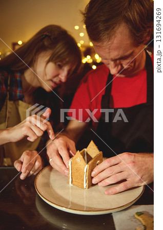 Friends Craft Gingerbread Houses Together in a Cozy Kitchen with Warm Holiday Lights Friends Craft Gingerbread Houses Together in a Cozy Kitchen with Warm Holiday Lights 131694269