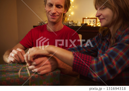Couple Unwraps Gift At Home During Christmas Evening With Cozy Lights And Plaid Shirts Couple Unwraps Gift At Home During Christmas Evening With Cozy Lights And Plaid Shirts 131694318