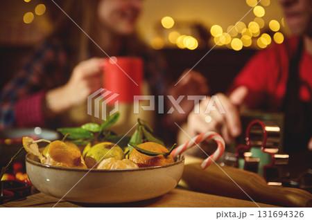 Friends At The Holiday Table: Cozy Christmas Scene With Citrus Bowl, Candy Cane, And Warm Fairy Lights 131694326