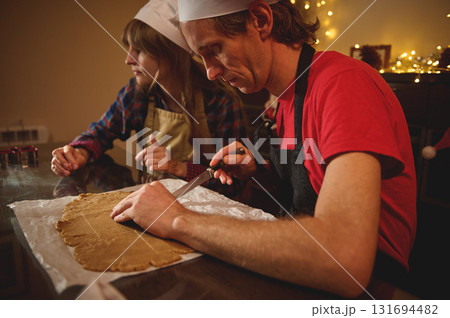 Two Cooks In Aprons Roll Dough For Christmas Treat As Festive Lights Glow In The Background 131694482