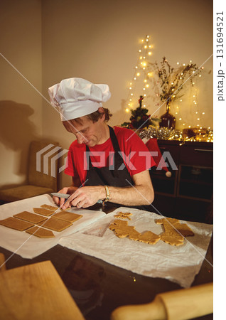 Chef In Christmas Kitchen: Baking Cookies At Home With Gingerbread Shapes And Warm Fairy Lights In The Background Chef In Christmas Kitchen: Baking Cookies At Home With Gingerbread Shapes And Warm Fairy Lights In The Background 131694521