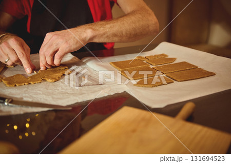 Home Baker Rolls And Cuts Dough On Parchment, Creating Small Rectangular Pieces For Baking In Warm Kitchen Home Baker Rolls And Cuts Dough On Parchment, Creating Small Rectangular Pieces For Baking In Warm Kitchen 131694523