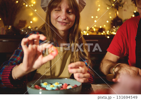 Happy Woman in Apron Decorating Cookies in Cozy Kitchen with Warm Fairy Lights and Festive Vibe Happy Woman in Apron Decorating Cookies in Cozy Kitchen with Warm Fairy Lights and Festive Vibe 131694549